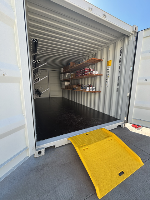 Organized shipping container with installed shelving, labeled storage boxes, and a yellow ramp for easy access—demonstrating how to organize a shipping container efficiently.
